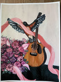 A rectangular art print  depicting a robin bird with spread wings resting on a wooden guitar, wrapped in a pink ribbon, with a bouquet of pink and purple flowers at the lower left, shown against a light background with a white border.