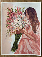 A rectangular art print featuring a painted woman in a pink dress holding a large bouquet of pink, white, and green flowers, shown against a light background with a white border. The print is photographed flat on a wooden surface.