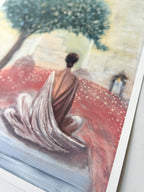 A close-up of a printed artwork showing a woman in a flowing dress seen from behind, standing in an outdoor scene under an olive tree. The print is photographed at an angle on a light surface. 