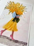 Anart print featuring a stylized illustration of a woman in a yellow skirt and pink high heels carrying a large bouquet of yellow flowers, shown against a pale pink background with a white border.